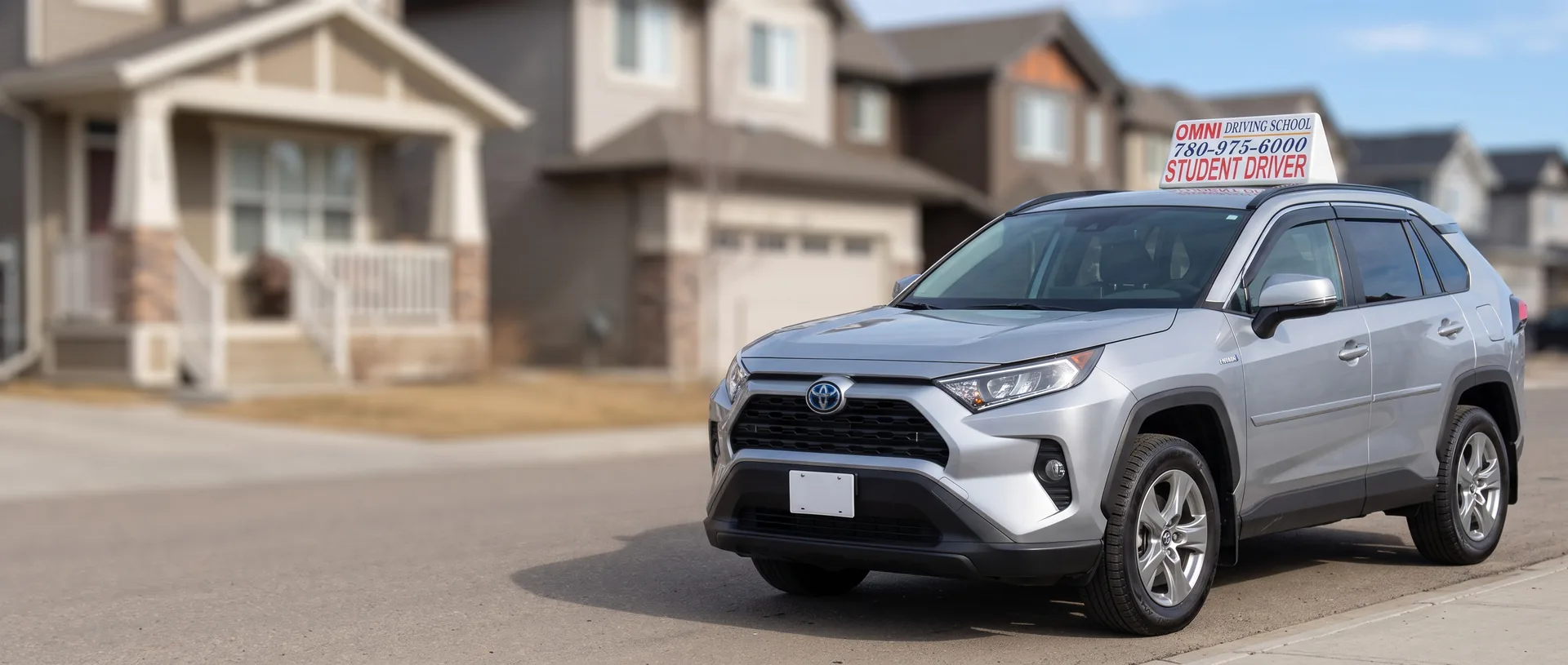 The Omni Driving School car with its roof sign, parked on a street of family homes